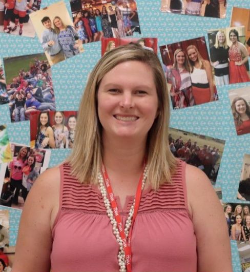 Walker standing in front of a board full of pictures with former students. Through the years Walker has taught, whenever a student took a picture with her, she placed it on the board. 