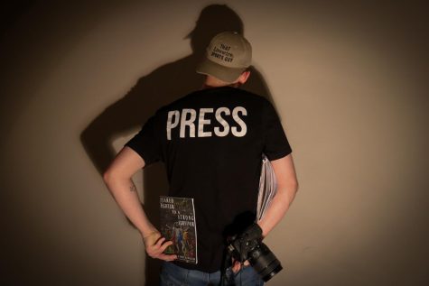 Senior Brodie Curtsinger wearing his Livewire Press shirt ,and his ‘That Livewire Sports Guy’ baseball cap, while also holding his camera equipment, his steno-pad used during interviews, and his recently published book that he is very proud of: “Feared Fighter To A Strong Survivor.”