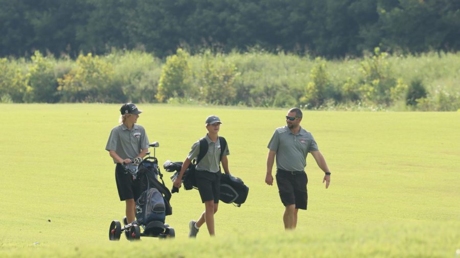 Coach Kyle Downs walking across the field alongside his players. The boys golf team has put in the effort to improve their skills this season. “The season is going very well right now. It is beyond our expectations from when we started,” coach Kyle Downs said.