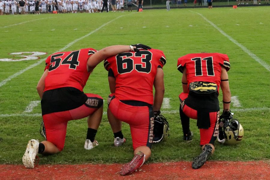 Seniors Tyler Redmon, Braxton Joslin, and junior Kayden Jenkins taking a knee in prayer before the game against Spencer County.